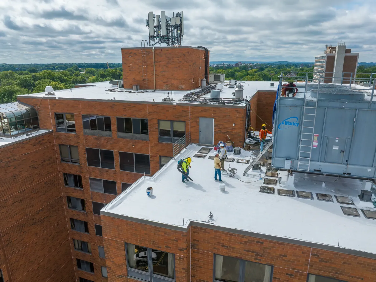 Roofing crew in safety gear working beside the cooling tower on the new white roof surface